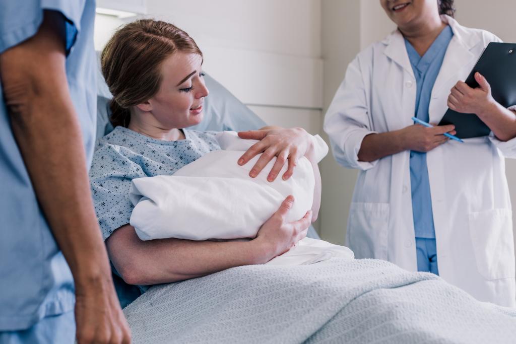 mother smiles as she holds newborn baby while resting in bed 1024x683 1